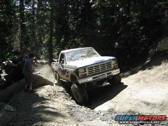 Ford pickup truck with lifted suspension navigating a dirt trail, kicking up dust. Driver is visible