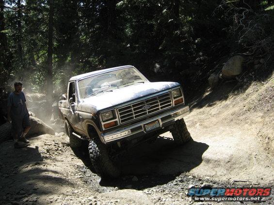 Ford pickup truck going off-road on a dirt trail with trees around. A person stands to the left