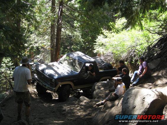 1986 Ford Bronco navigating a steep, rocky off-road trail with several people watching