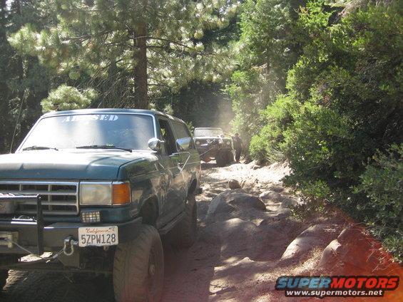 Green Ford Bronco on a rocky trail, front bumper with winch and license plate visible