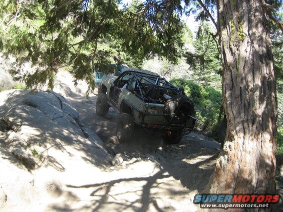 Off-road vehicle with a roll cage climbing a rocky trail, another vehicle behind it