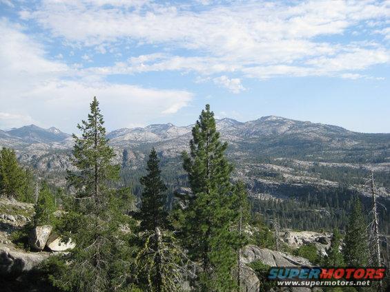 Mountainous terrain with scattered pine trees under a partly cloudy sky