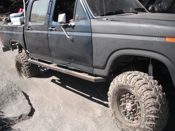side view of dark blue pickup truck with large off-road tires and metal running boards on a rocky surface