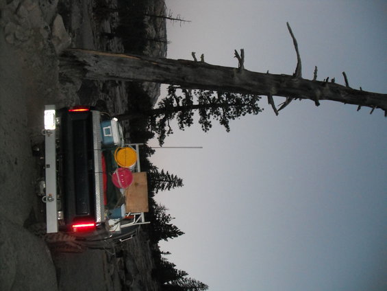 Rear view of a truck bed loaded with yellow and red buckets, a cooler, and other gear, parked on a dirt road