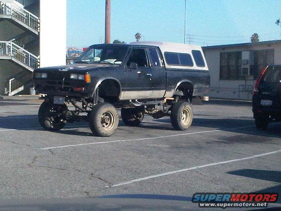 Lifted black pickup truck with white camper shell, seen from 3/4 front