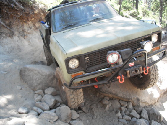 Olive green off-road vehicle with winch and auxiliary lights climbing over rocks
