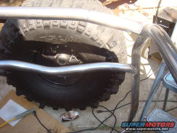 Roll cage tubing welded around a large off-road tire. Some tools and a crushed can are on the ground