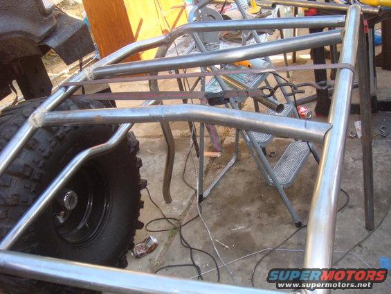 Metal tubing for a roll cage is being welded and assembled next to a large off-road tire