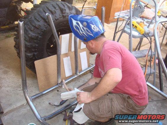 Guy in welding mask working on metal tubing near a giant tire
