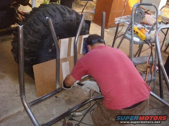 Roll cage being welded around a large off-road tire. A man in a red shirt is welding