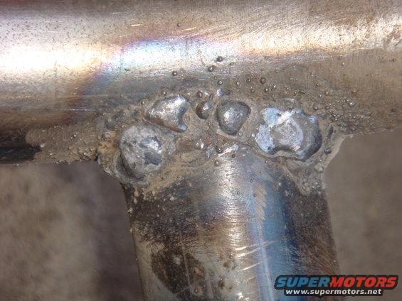 Close-up of rough welds on shiny metal tubing, with some dirt and discoloration