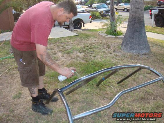 Man sprays metal roll cage with white paint