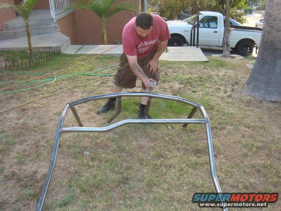 Man spraying a metal roll cage with a can of spray paint outdoors