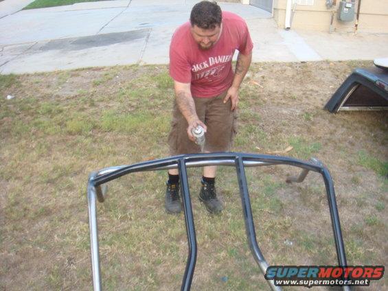man spraying black paint on metal roll cage