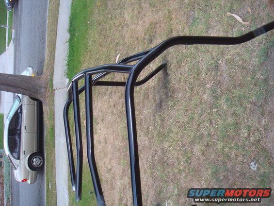 Black roll cage tubes in foreground, beige sedan parked on street in background