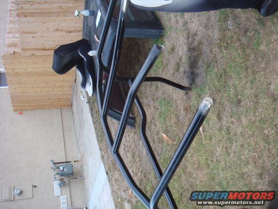 Black roll cage tubing with cut ends, lying on grass next to a wooden fence