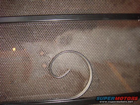 Close-up of a metal mesh screen with a curved metal trim piece on it. Supermotors.net logo visible