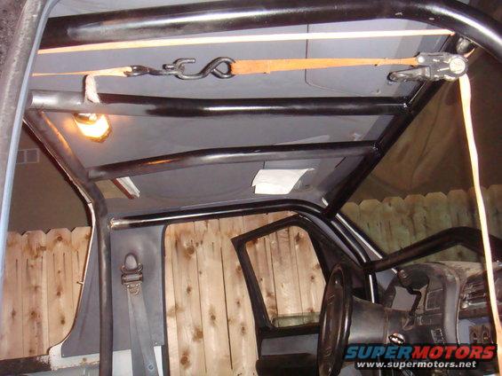 Interior view of a vehicle with a custom roll cage installed, showing the headliner, door panel, and steering wheel