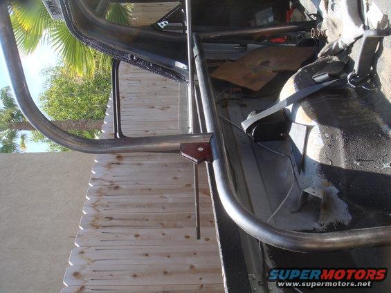 Roll cage tubing inside a vehicle, with a wooden fence and palm trees visible outside