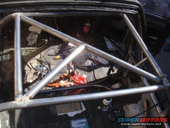 Roll cage inside a vehicle interior, with tools and a bottle of Coca-Cola visible