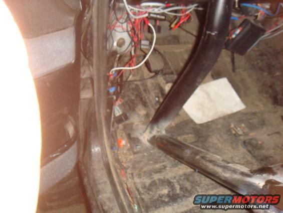 Interior shot of a vehicle showing a roll cage and a mess of wires and electrical components on the floor