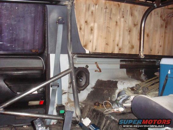 Interior view of a vehicle with a roll cage, speaker, and seatbelt