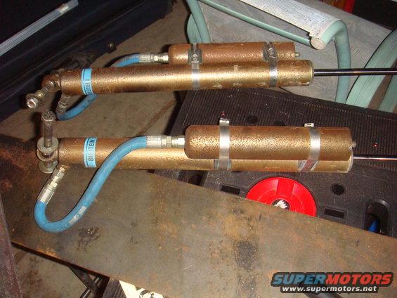 Two rusty Bilstein shock absorbers with blue hoses, mounted on a workbench