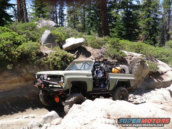 Modified pickup truck with roll cage and spare tire off-roading on rocky terrain