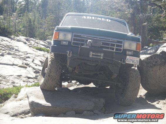 Green off-road vehicle with "ABUSED" sticker on windshield, navigating rocky terrain