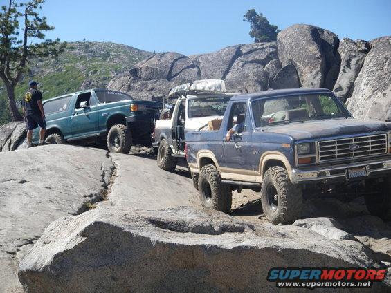 Blue 1980s Ford Bronco, green Ford Bronco, and white pickup truck on a rocky off-road trail