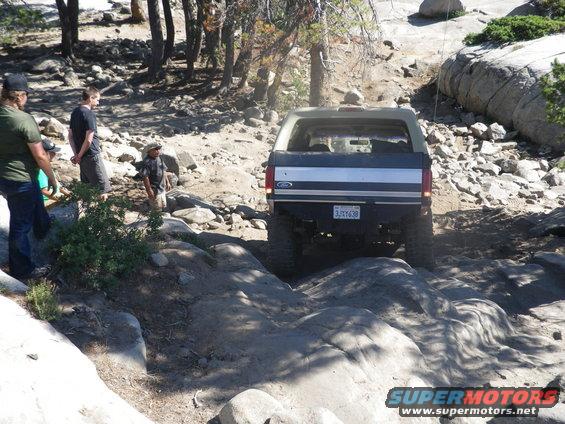 Ford Bronco driving on a rocky trail, rear view. Two-tone paint, license plate visible