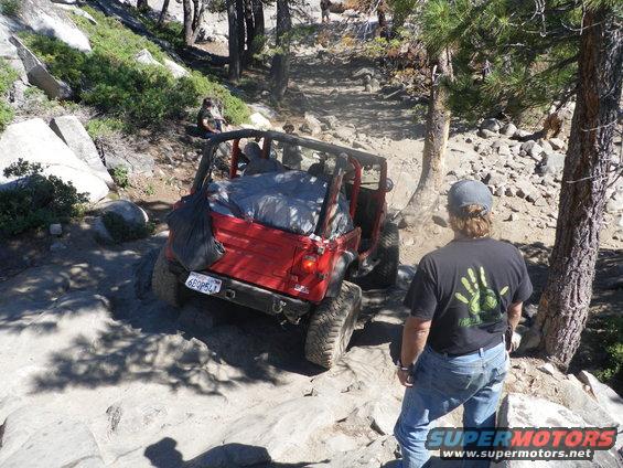 Red Jeep Wrangler on rocky trail, rear view, license plate 6BQP541