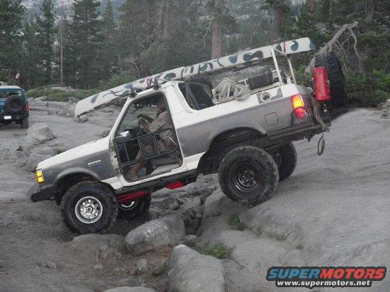 White and grey 1991 Ford Bronco off-roading with a canoe on the roof rack