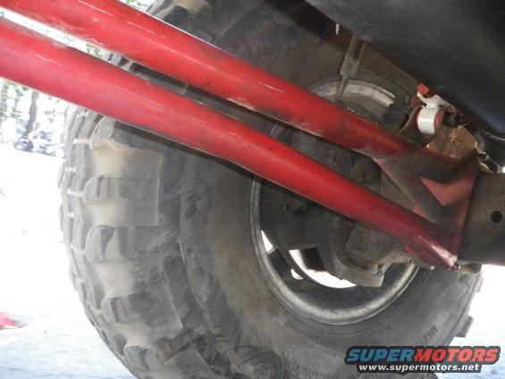 Red suspension arms above a large, knobby tire on a vehicle. Text 'SUPERMOTORS' visible