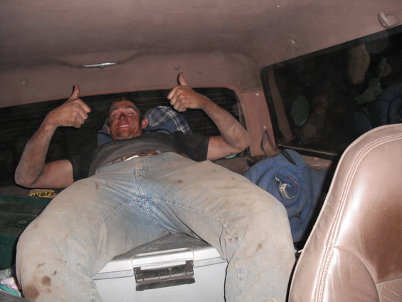 Man with dirty face and jeans gives two thumbs up from inside a vehicle's rear compartment