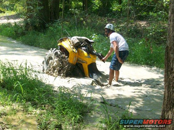 Yellow Can-Am ATV stuck in mud, person attempting to pull it out