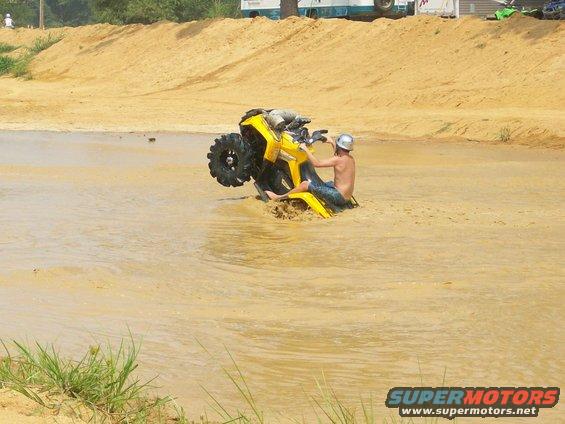 Person on a yellow ATV stuck in muddy water with one wheel up