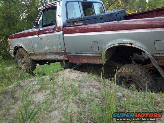 Maroon and silver Ford pickup truck stuck in mud, side view