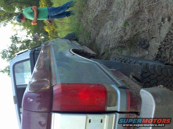 1987 Ford F-150 rear quarter panel and taillight, stuck in mud with a person standing nearby