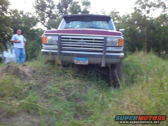 Front view of a maroon Ford F-150 truck with a brush guard, parked on a grassy incline