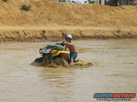 Guy on yellow ATV stuck in muddy water, wearing helmet and shorts