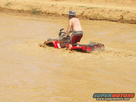 Red ATV stuck in mud with a person riding it