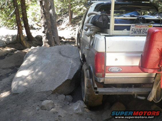 Ford Bronco navigating a tight spot next to a large boulder on a wooded trail
