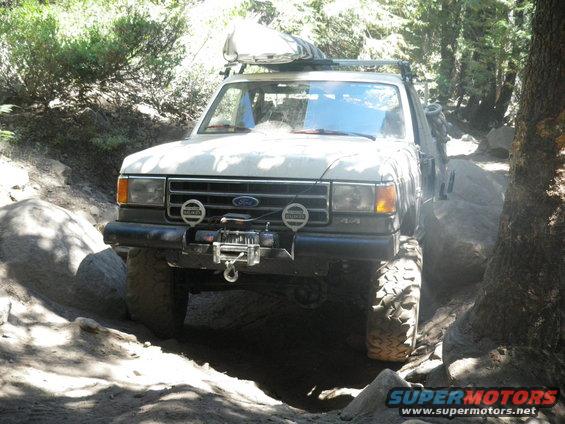 White 1991 Ford Bronco on a rocky trail with a winch and roof rack