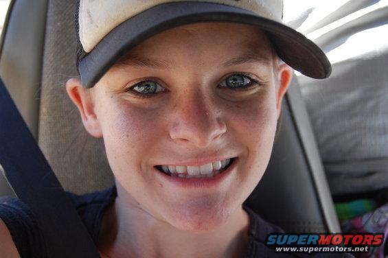 Close-up of a smiling person wearing a baseball cap and a seatbelt