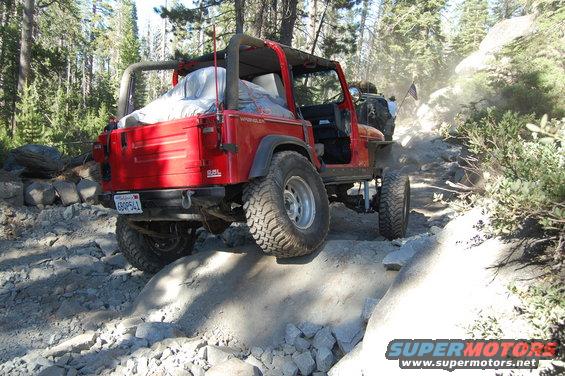 Red 1993 Jeep Wrangler navigating a rocky off-road trail, rear view