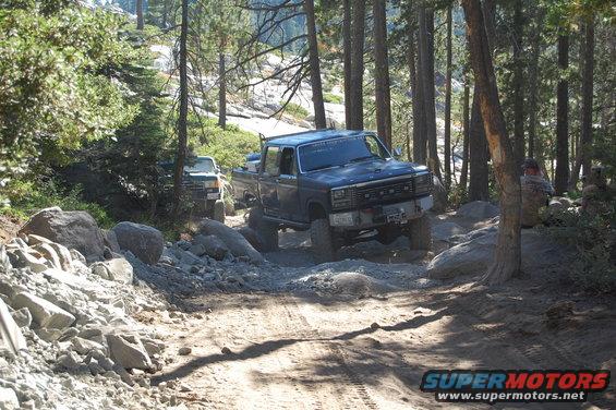 Ford pickup truck driving on a rocky trail with another truck behind it