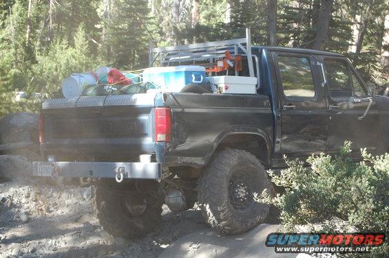 Rear view of a black pickup truck with a rack in the bed, loaded with camping gear and a cooler. License plate reads LGT803