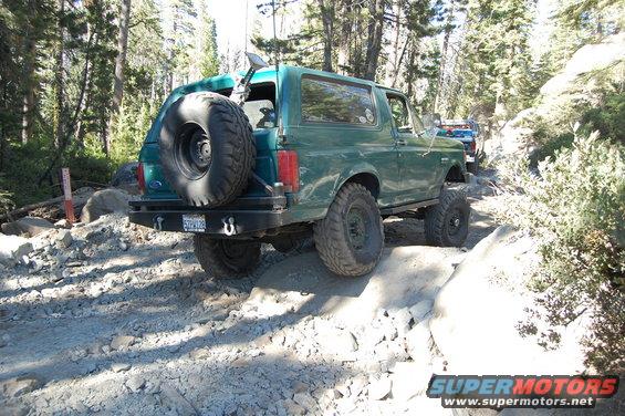 Green SUV with spare tire on rear, driving on rocky terrain