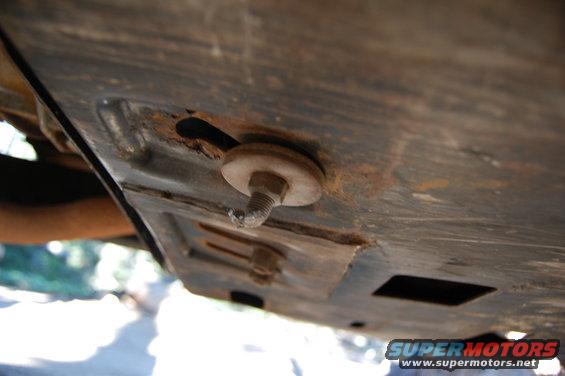 Underside of a vehicle with a rusty bolt and washer attached to a metal plate
